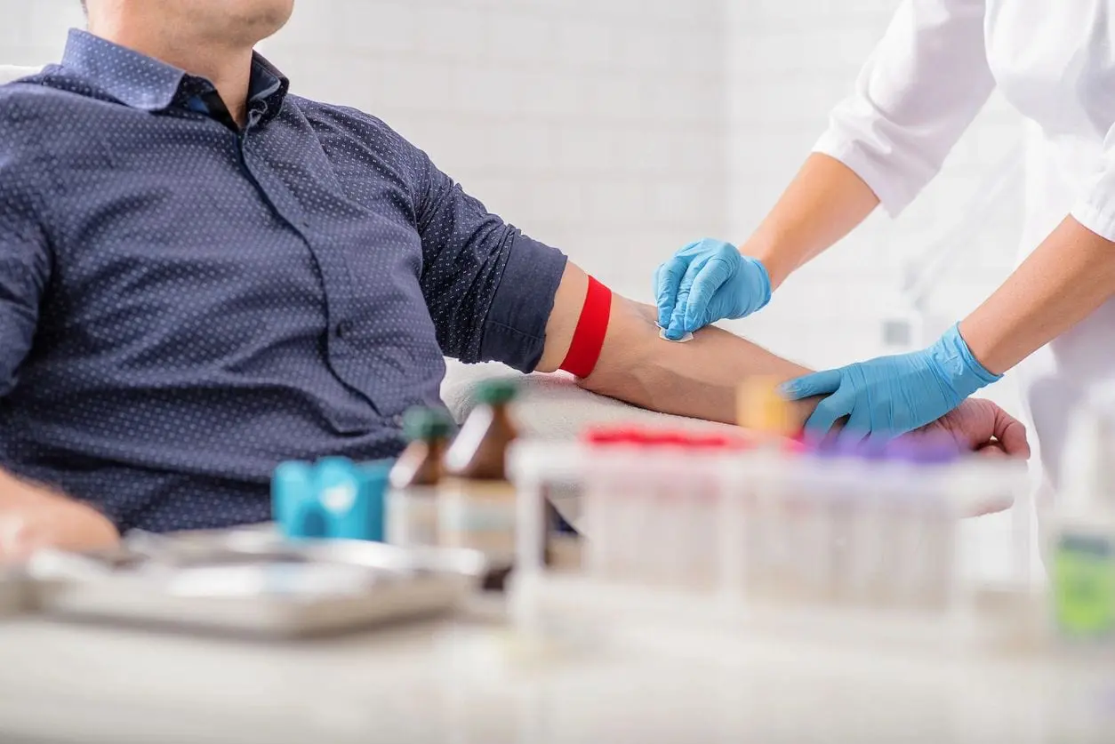 White man in a polka-dotted blue shirt having a medical professional clean his arm for a blood donation
